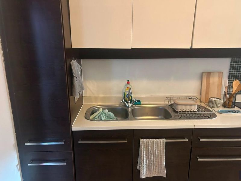 A functional kitchen area featuring dark wood cabinetry, a double bowl stainless steel sink, and a tiled backsplash.
