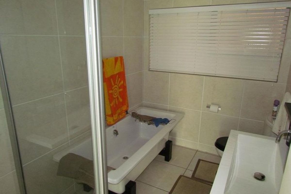 A functional bathroom featuring a bathtub, separate shower enclosure, and a modern vanity basin with neutral wall and floor tiling.