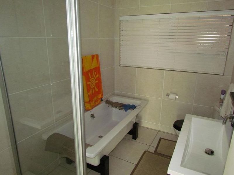 A functional bathroom featuring a bathtub, separate shower enclosure, and a modern vanity basin with neutral wall and floor tiling.