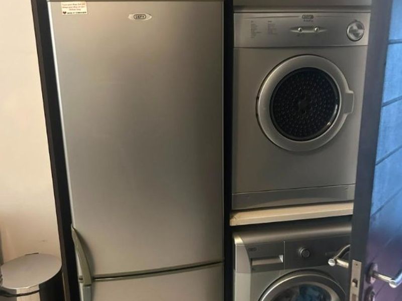 A compact laundry area featuring built-in cabinetry designed to house a refrigerator, washing machine, and tumble dryer.