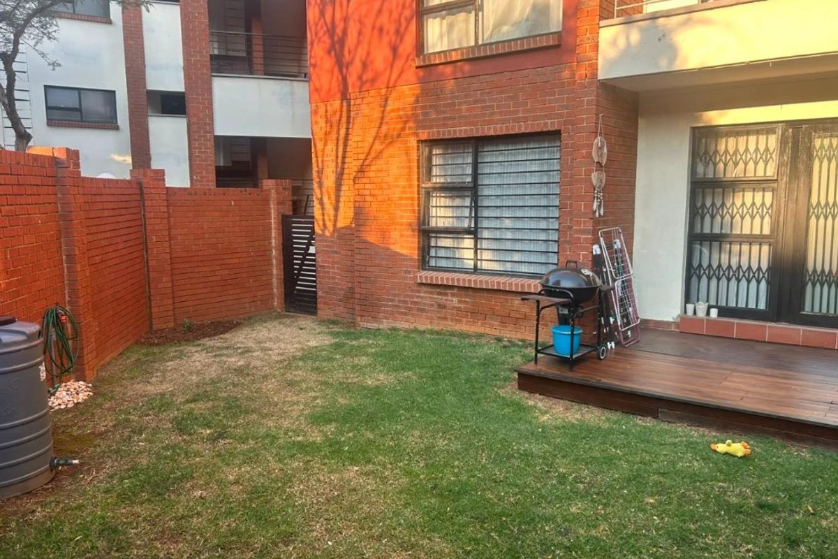 A private rear garden area featuring a timber deck, brick boundary walls, and direct access to the apartment through a security gate.
