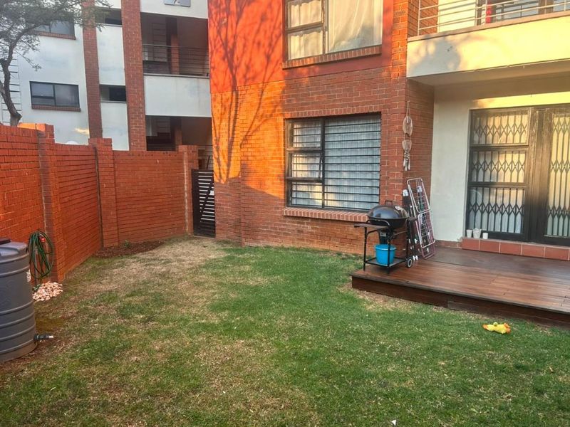 A private rear garden area featuring a timber deck, brick boundary walls, and direct access to the apartment through a security gate.