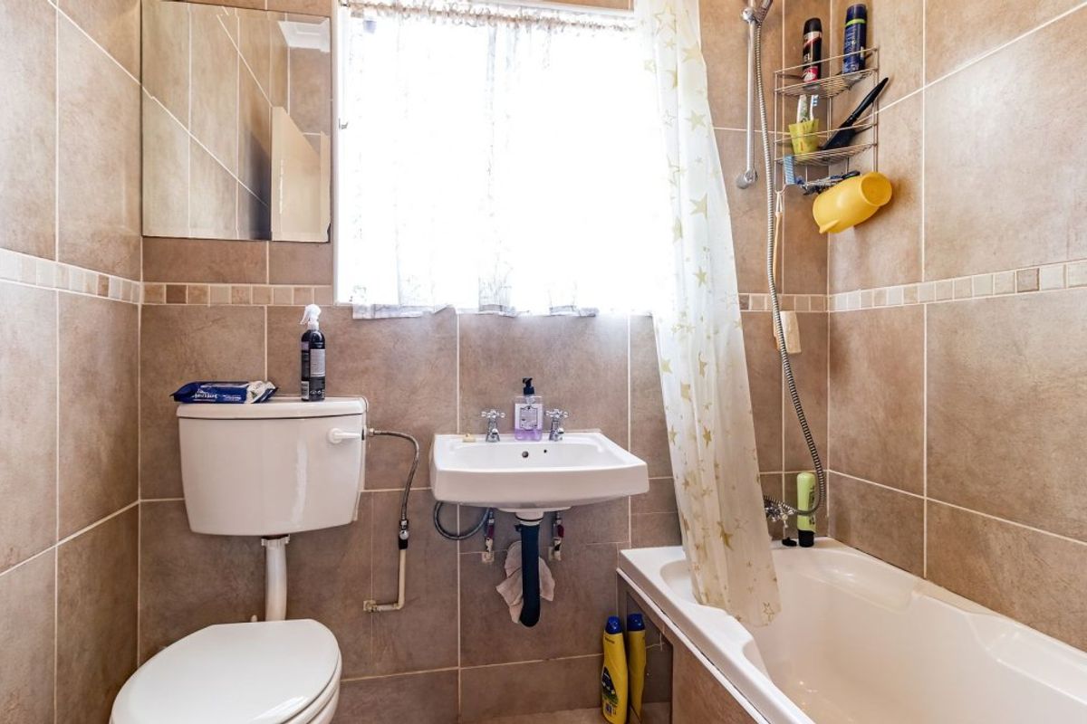 A functional bathroom featuring tiled walls, a wall-mounted basin, a toilet, and a bathtub with a shower attachment.
