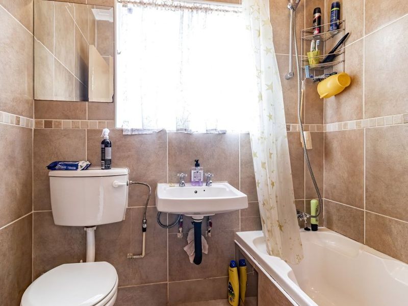 A functional bathroom featuring tiled walls, a wall-mounted basin, a toilet, and a bathtub with a shower attachment.