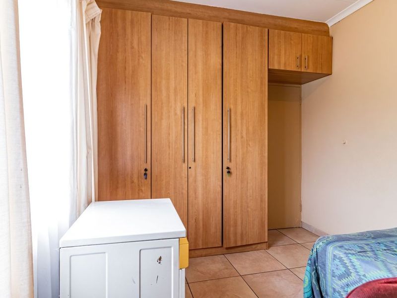 A bedroom featuring built-in wooden cupboards with overhead storage and tiled flooring.