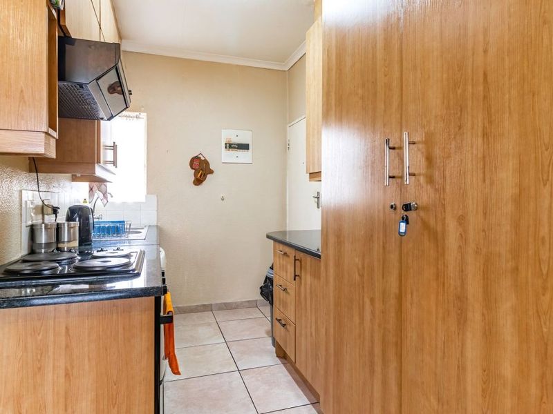 A functional kitchen featuring wood-look laminate cabinetry, dark granite countertops, an electric hob with extractor fan, and tiled flooring.