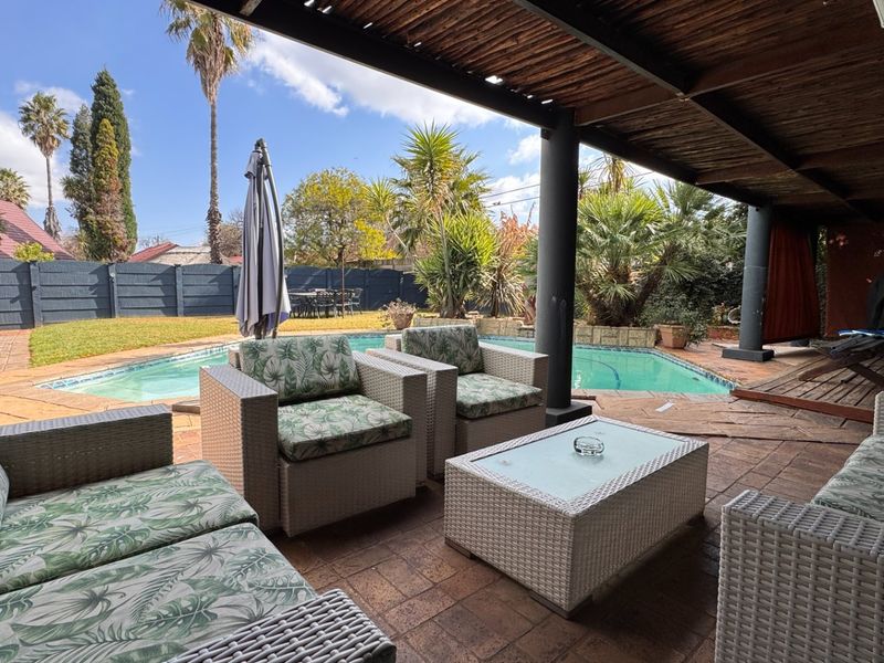 Covered outdoor patio area featuring a timber pergola, paved flooring, and direct access to a private swimming pool and garden.