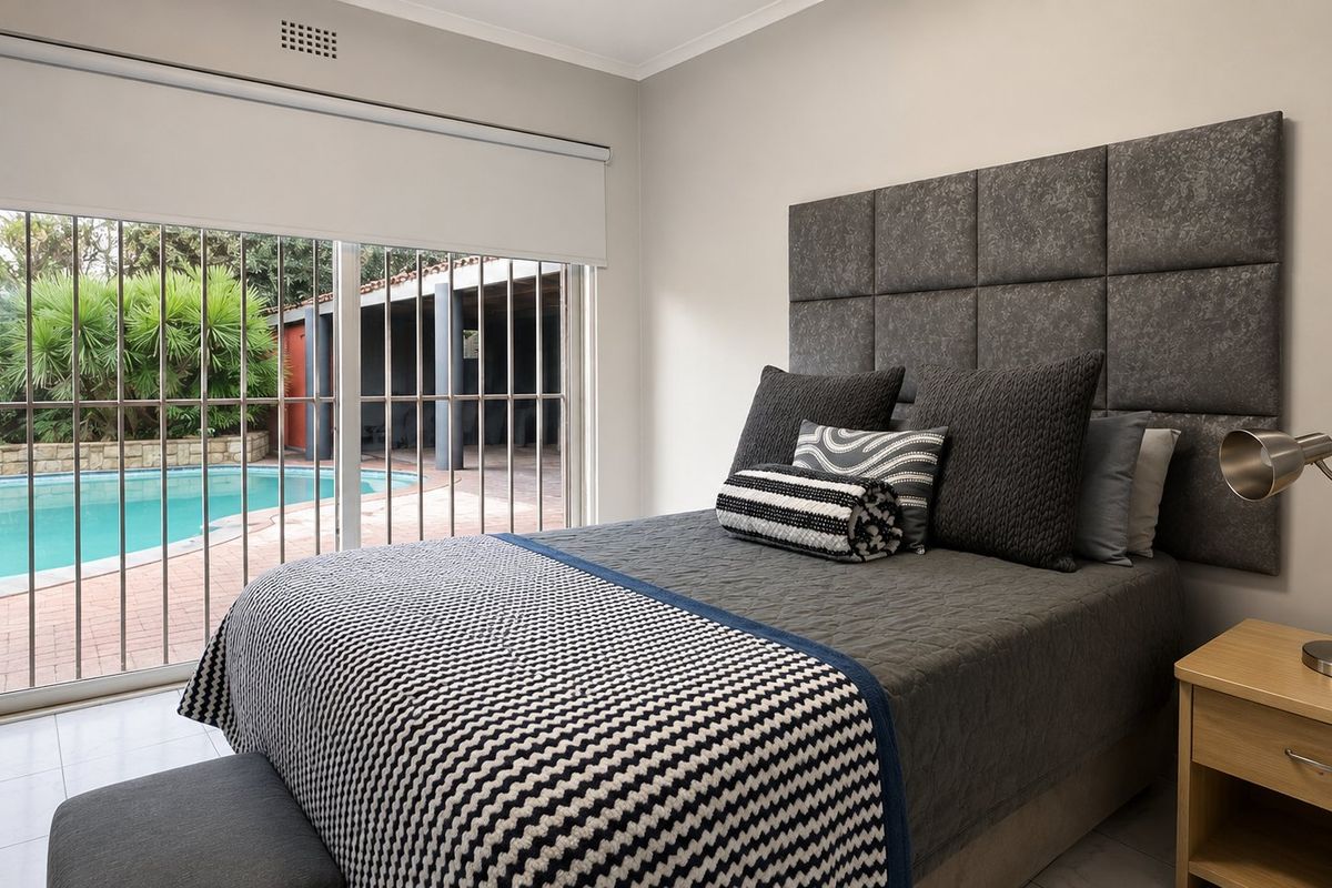 A well-maintained bedroom featuring a large sliding glass door with security bars, providing direct access to the outdoor pool area.