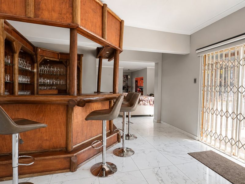 A dedicated bar area featuring a custom wooden bar counter with integrated shelving and modern marble-look floor tiles, leading to an outdoor security gate.