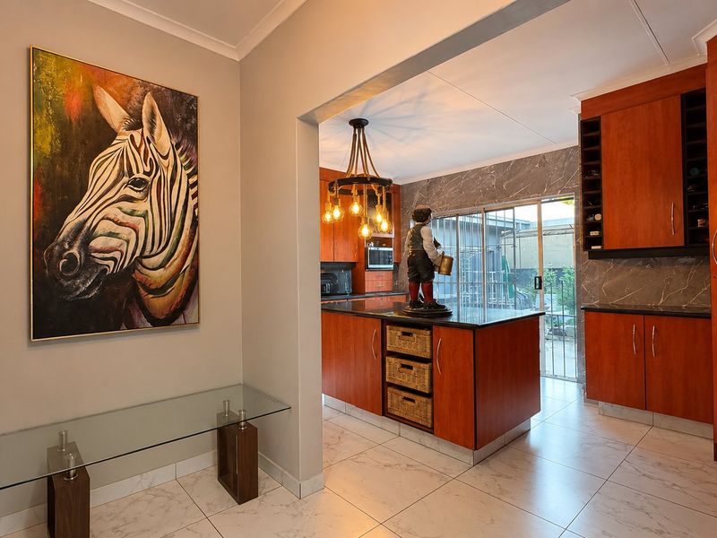 A well-maintained kitchen featuring warm-toned wooden cabinetry, a central island with stone countertops, and modern marble-look floor tiles with direct access to the outdoors.