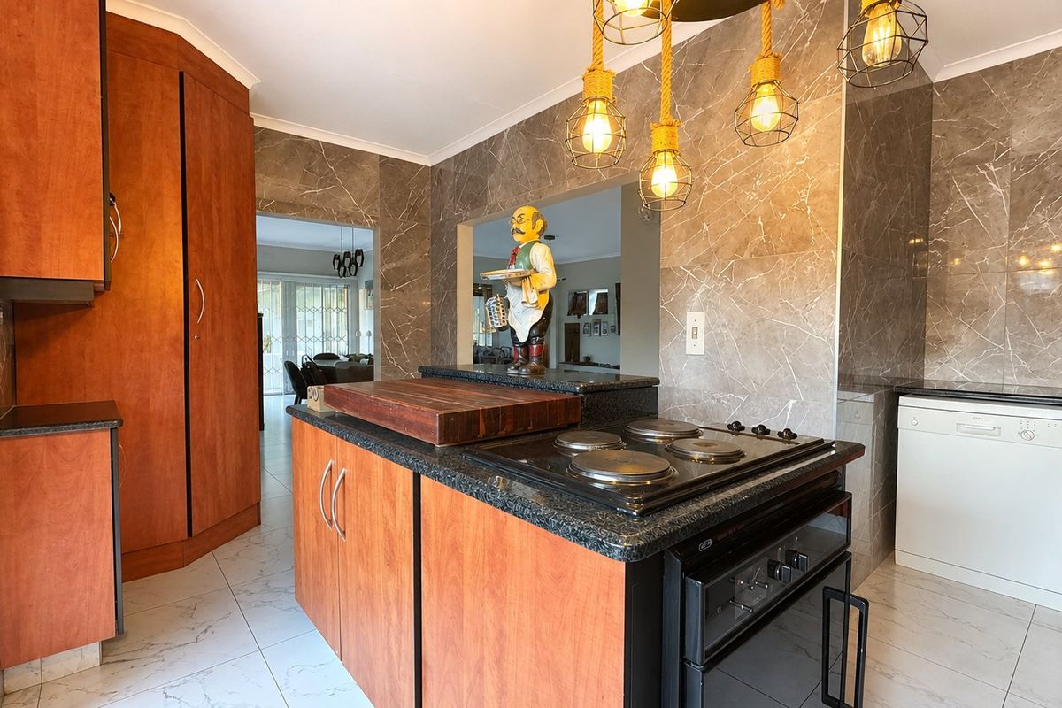 A functional kitchen featuring wood-finish cabinetry, granite countertops, an integrated electric hob and oven, and modern marble-look wall tiling.