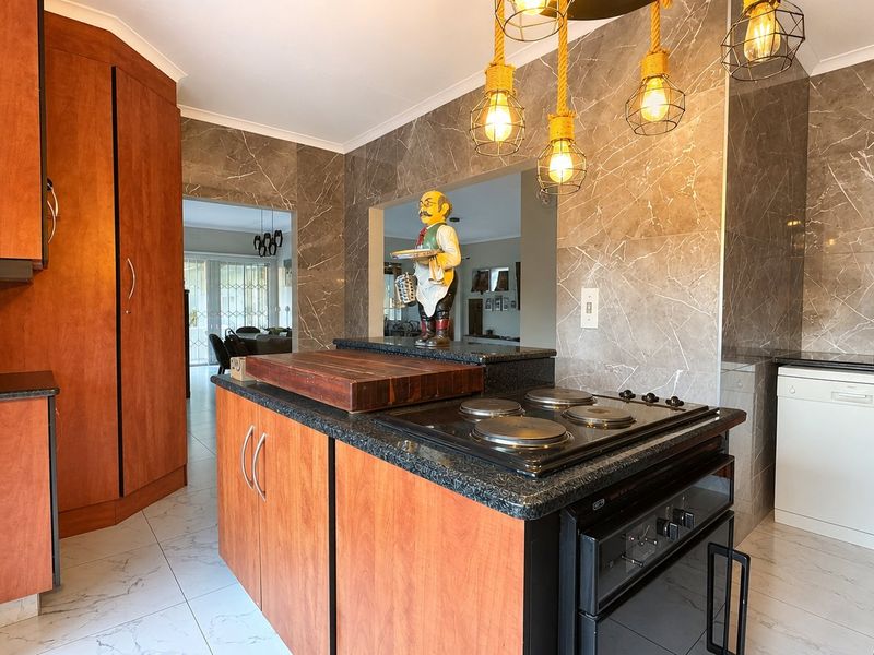 A functional kitchen featuring wood-finish cabinetry, granite countertops, an integrated electric hob and oven, and modern marble-look wall tiling.
