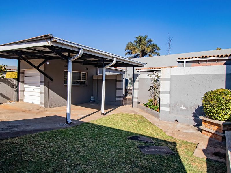Front exterior view featuring a covered carport, garage access, and a paved driveway with surrounding boundary walls.