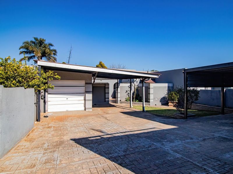Front exterior view featuring a paved driveway, a single garage, and a covered carport area with surrounding boundary walls.