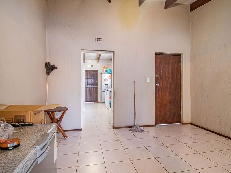 An open-plan living area featuring tiled flooring and exposed timber ceiling beams, leading through to a secondary kitchen or utility space.