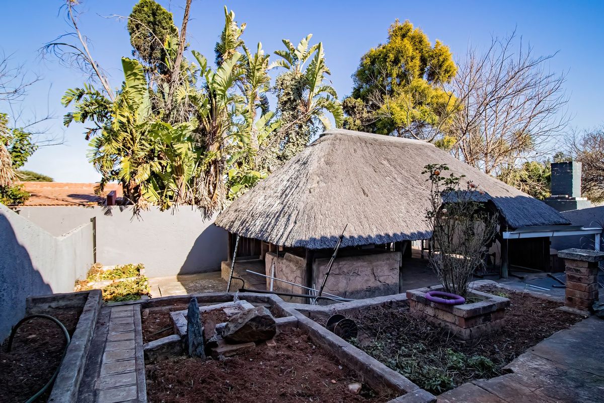 Rear garden area featuring a traditional thatched roof structure, masonry boundary walls, and established raised brick garden beds requiring maintenance.