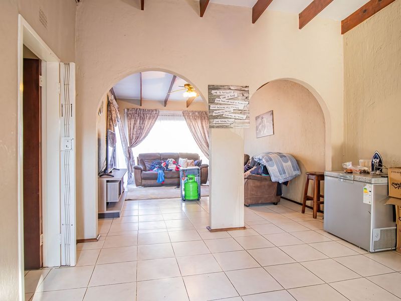 Open plan living area featuring exposed timber ceiling beams, ceramic floor tiles, and arched architectural details connecting the lounge and dining spaces.