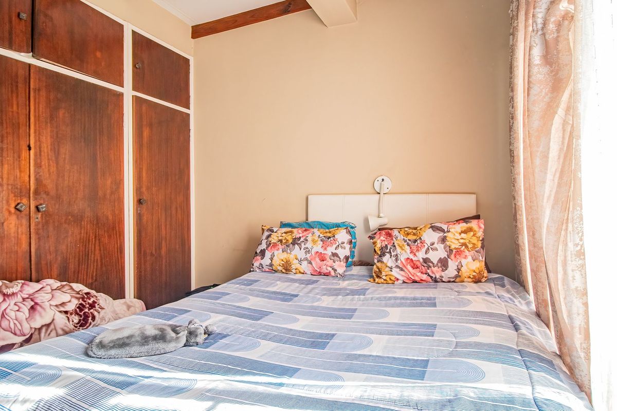 A compact bedroom featuring built-in wooden cupboards and an exposed ceiling beam, offering a functional space with potential for modern updates.