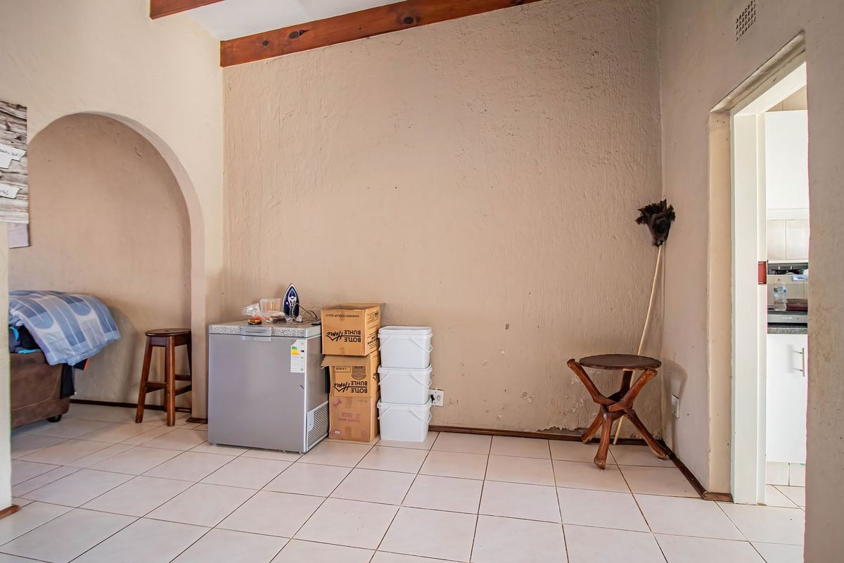 A living area featuring ceramic floor tiles, exposed timber ceiling beams, and an arched doorway leading to adjacent spaces.