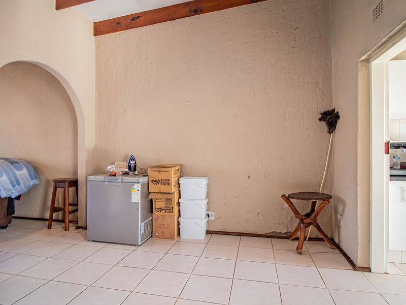 A living area featuring ceramic floor tiles, exposed timber ceiling beams, and an arched doorway leading to adjacent spaces.
