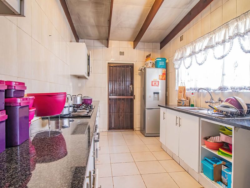 A functional kitchen featuring granite countertops, gas hob, built-in cabinetry, and exposed timber ceiling beams, offering a practical layout with direct exterior access.