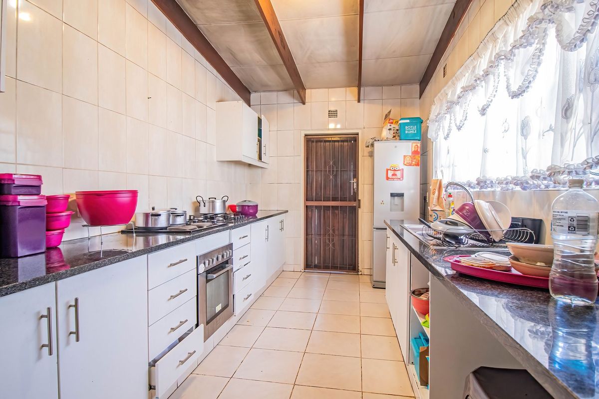 A functional galley-style kitchen featuring granite countertops, built-in oven, gas hob, and tiled finishes, offering a practical layout with direct exterior access.