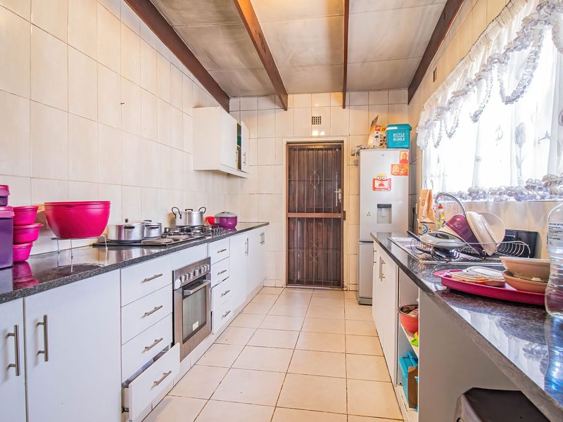 A functional galley-style kitchen featuring granite countertops, built-in oven, gas hob, and tiled finishes, offering a practical layout with direct exterior access.