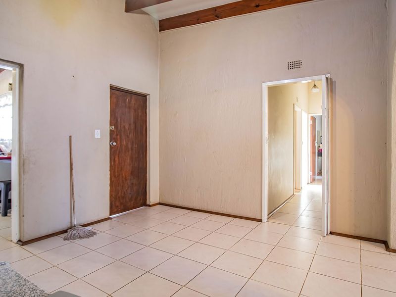 An open-plan living area featuring ceramic floor tiles, exposed timber ceiling beams, and an arched entryway leading to a hallway.