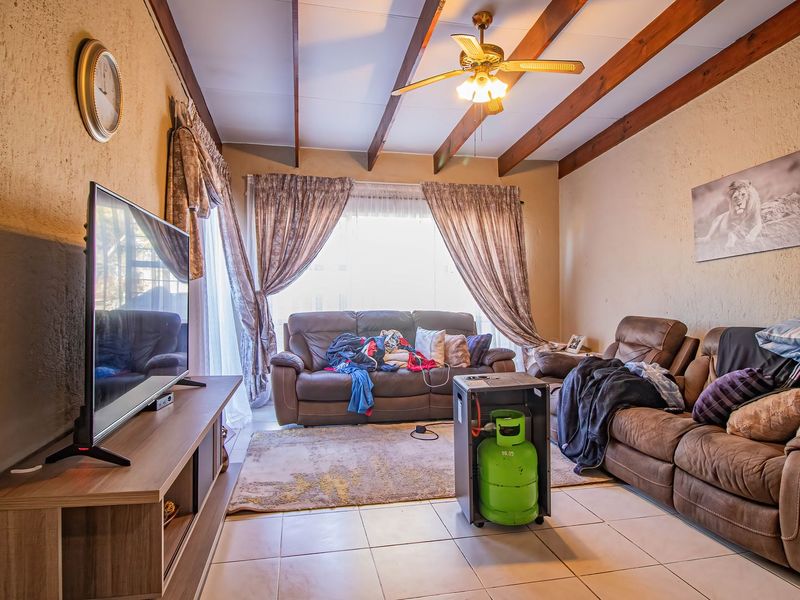 A living room featuring exposed timber ceiling beams, a ceiling fan, and tiled flooring, offering a comfortable and functional space.