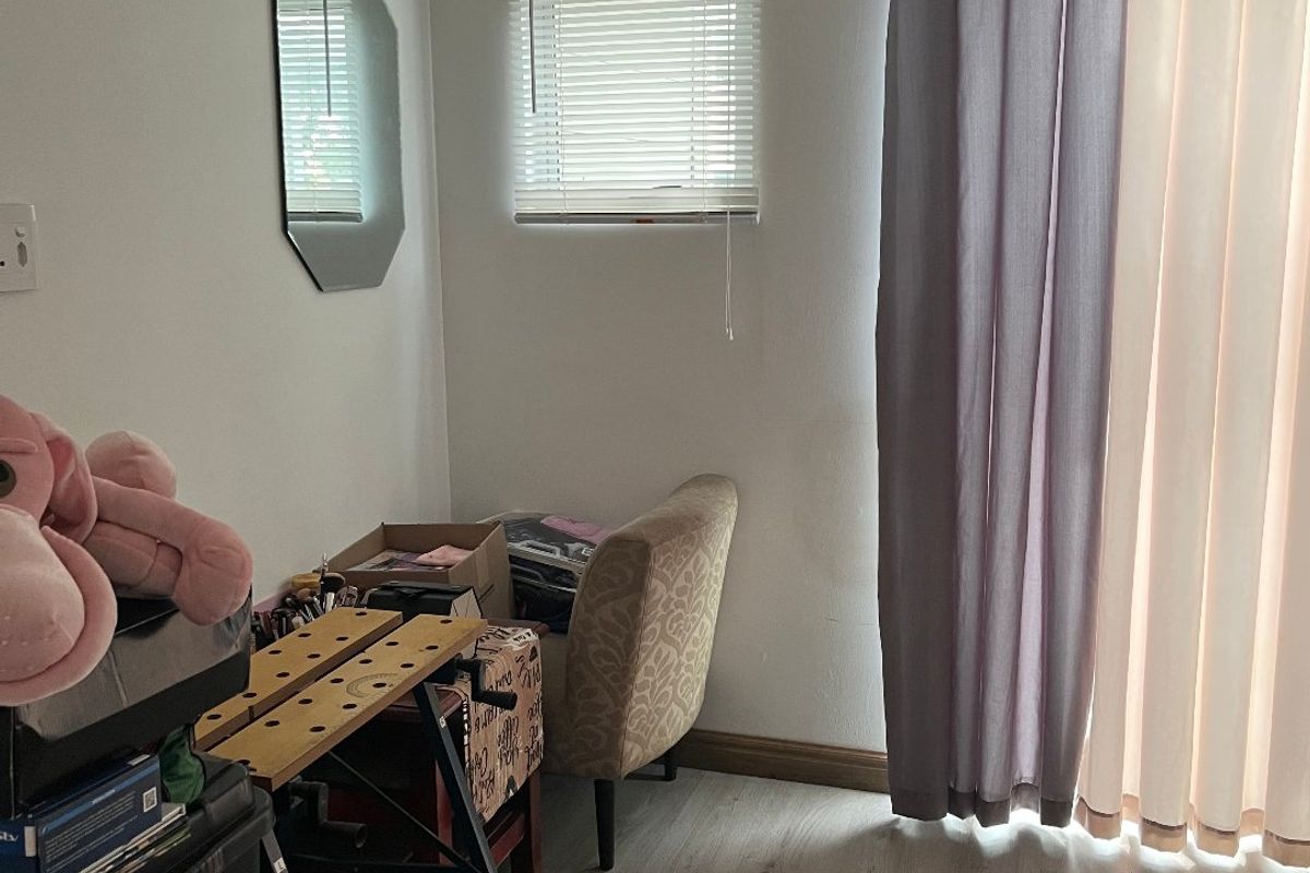 A bedroom featuring light-toned laminate flooring, recessed ceiling lighting, and a window fitted with venetian blinds and curtain rods.