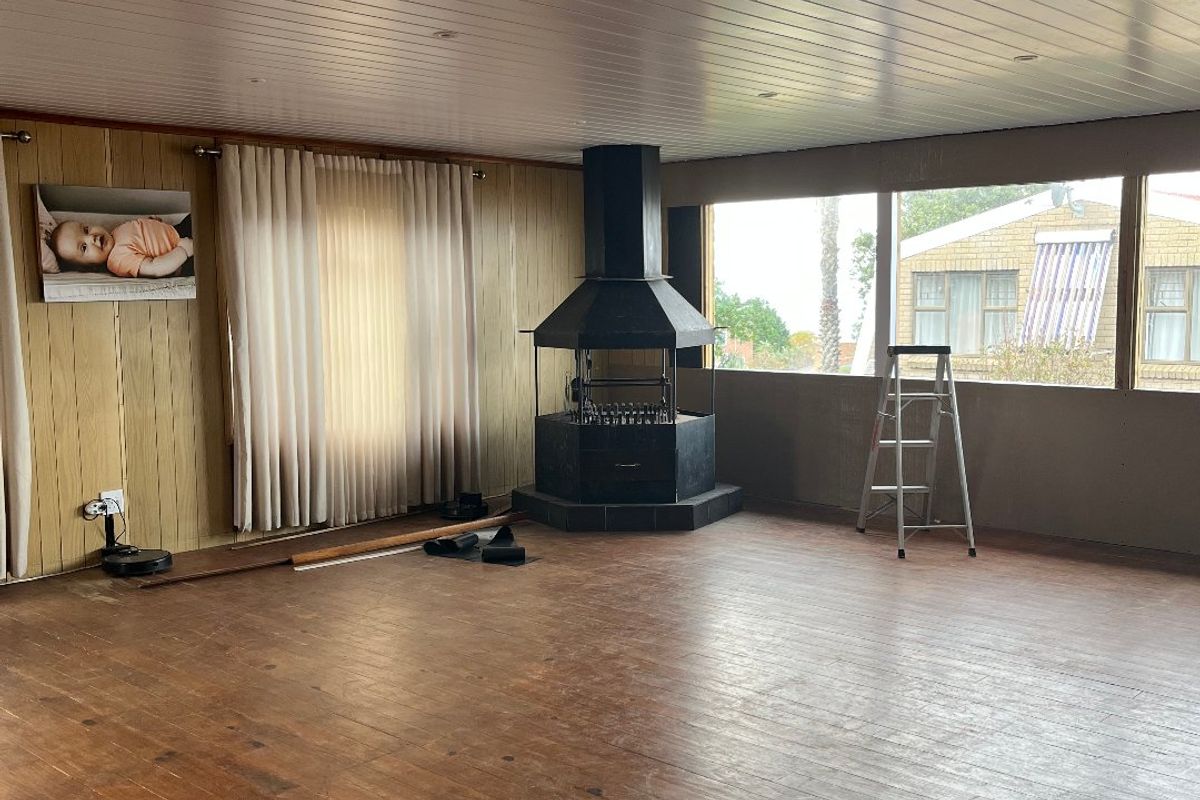 Spacious living area featuring timber flooring, wood-panelled ceiling, and a central freestanding fireplace, offering a blank canvas for renovation.