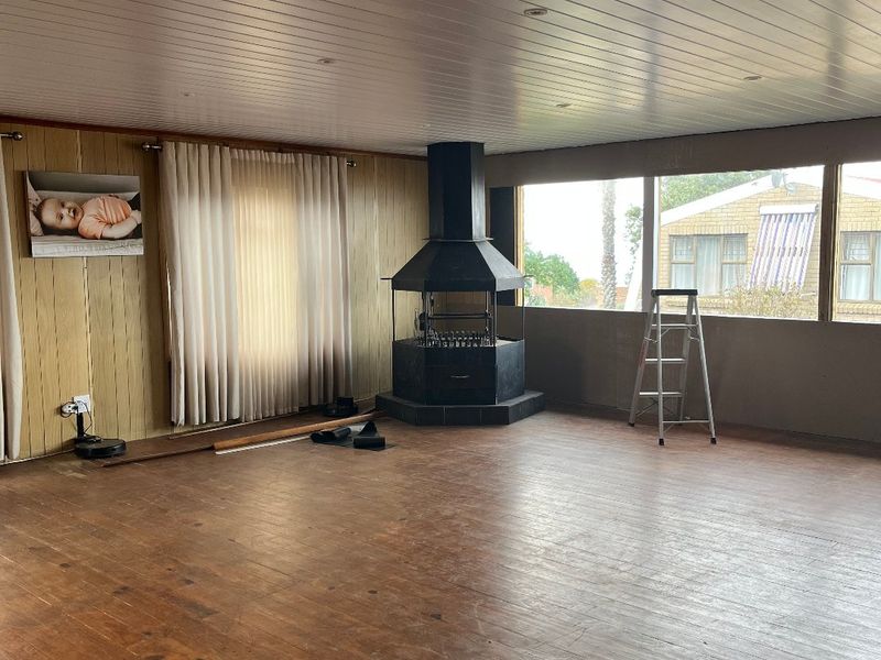 Spacious living area featuring timber flooring, wood-panelled ceiling, and a central freestanding fireplace, offering a blank canvas for renovation.