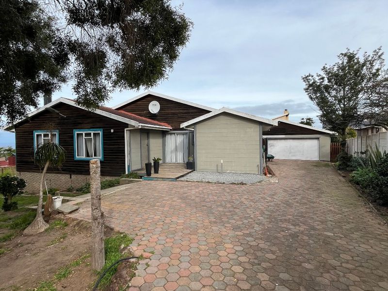 Front elevation of a house featuring a paved driveway, attached garage, and timber-clad facade with a concrete block entrance section.