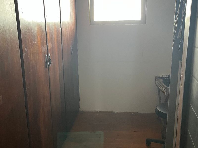 A small bedroom featuring extensive built-in wooden cabinetry and timber flooring, requiring cosmetic updates to improve the overall finish and appeal.