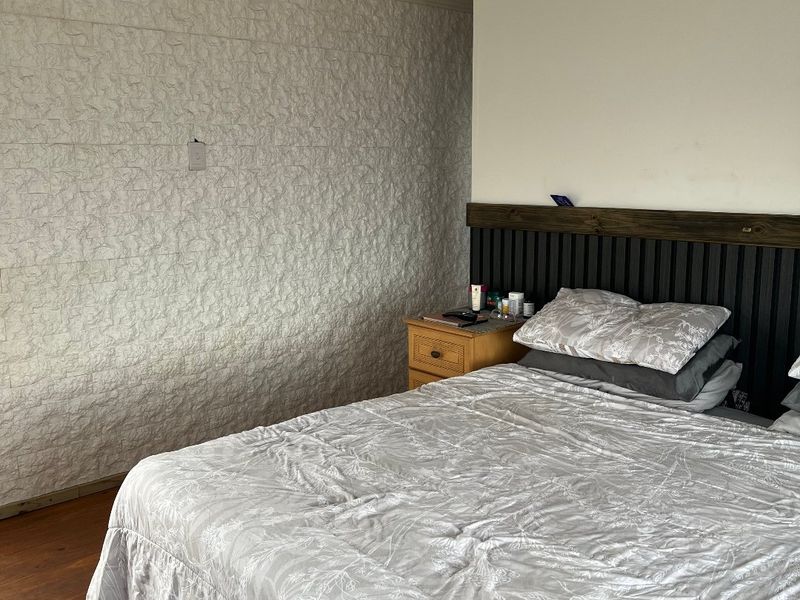 A bedroom featuring timber flooring, a textured feature wall, and a custom timber panel headboard under a tongue and groove ceiling.