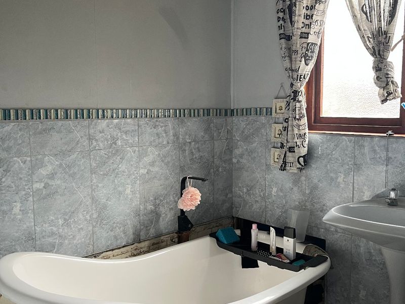 Bathroom featuring a freestanding bathtub, pedestal basin, and marble-effect wall tiling with a decorative border.