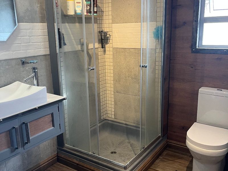 Modern bathroom featuring a glass shower enclosure, vessel sink with vanity cabinet, toilet, and contemporary wood-look floor tiling.