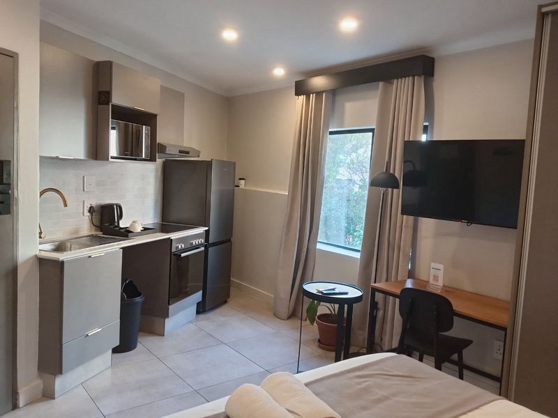 Modern open-plan studio apartment featuring a compact kitchenette with built-in appliances, tiled flooring, and recessed lighting.