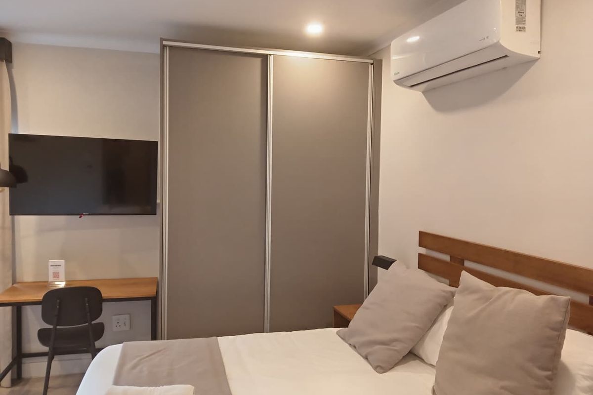 A well-maintained bedroom featuring a built-in sliding wardrobe, wall-mounted air conditioning unit, and recessed ceiling lighting.