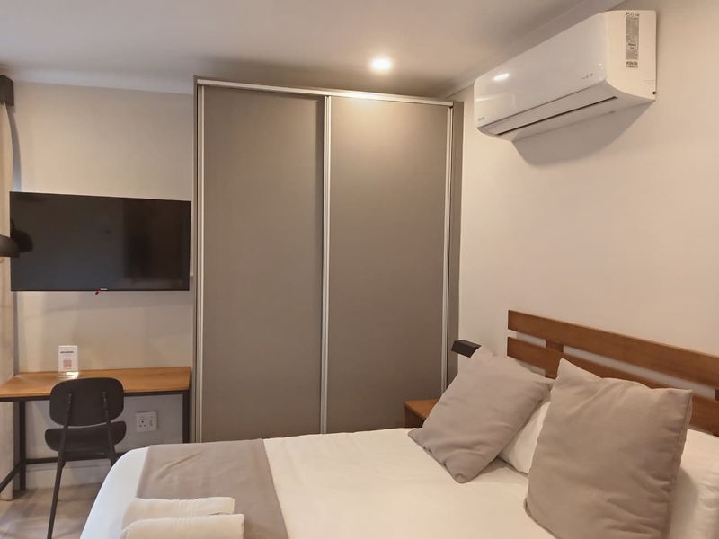 A well-maintained bedroom featuring a built-in sliding wardrobe, wall-mounted air conditioning unit, and recessed ceiling lighting.