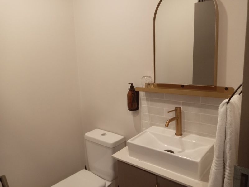 A modern guest bathroom featuring a sleek vanity with a vessel sink, brass fixtures, subway tile backsplash, and an arched mirror.
