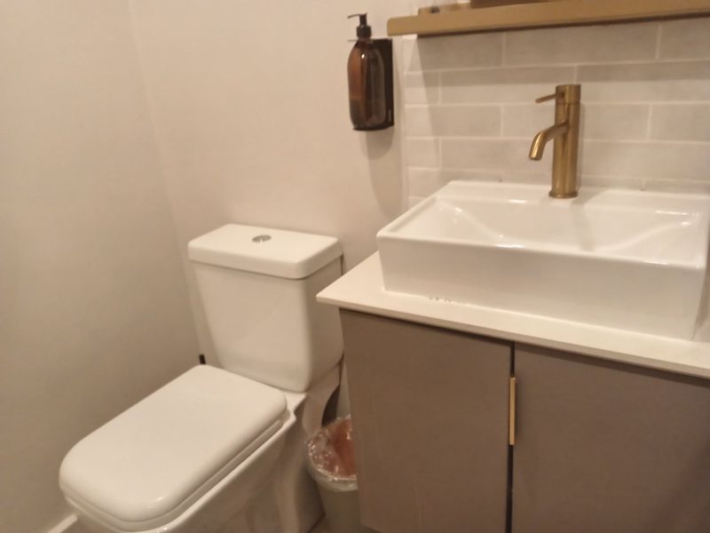 A modern bathroom featuring a vanity with a vessel sink, brass faucet, subway tile backsplash, and a white toilet.