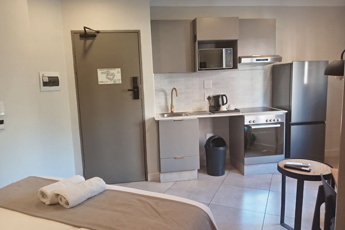 Compact open-plan studio apartment featuring a modern kitchenette with built-in cabinetry, stainless steel appliances, and tiled flooring.