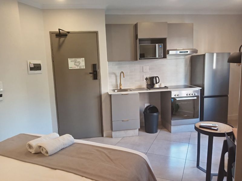 Compact open-plan studio apartment featuring a modern kitchenette with built-in cabinetry, stainless steel appliances, and tiled flooring.