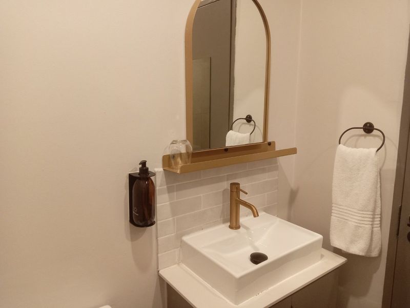 A modern bathroom vanity area featuring a white basin, brass faucet, subway tile backsplash, and an arched mirror with a built-in shelf.