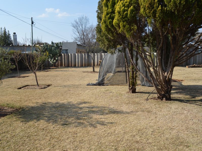 A spacious residential garden featuring a lawn, mature trees, and a perimeter precast concrete wall.