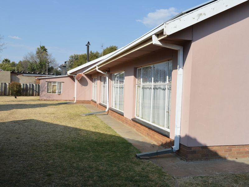 Rear view of the house showing the exterior wall, metal-framed windows, and guttering system set against a lawn area.