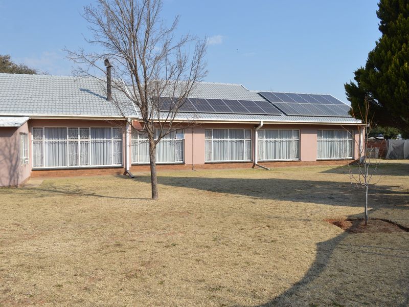 Rear view of the house featuring a tiled roof with installed solar panels, brick exterior walls, and large windows overlooking the garden.