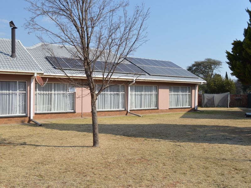 Rear view of the house featuring a metal roof with installed solar panels, brick base, and large windows with security bars.