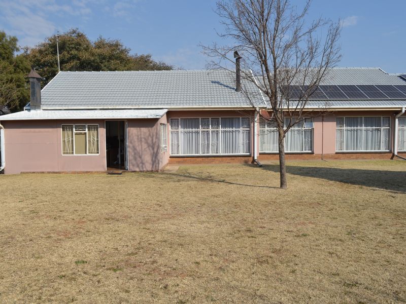 Rear view of the house featuring a tiled roof, solar panels, and a spacious lawn area.